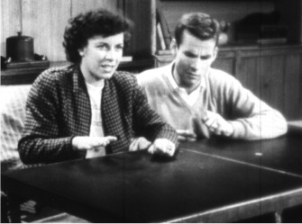 A woman and a man seated at a table, watching off camera.